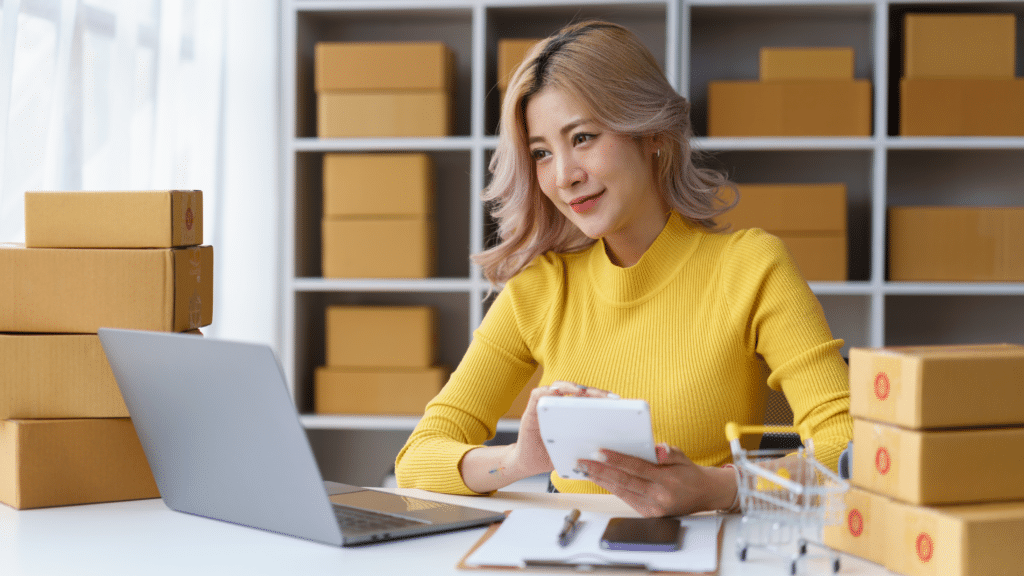 Small business owner managing inventory with laptop and phone to track products and prevent stock discrepancies.