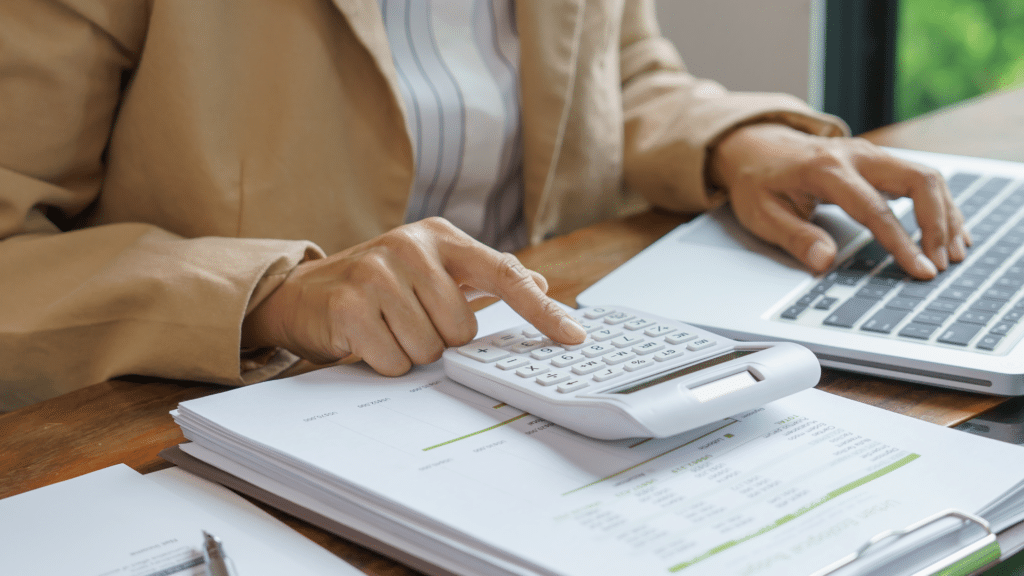 Person calculating finances with documents and laptop during financial statement analysis.